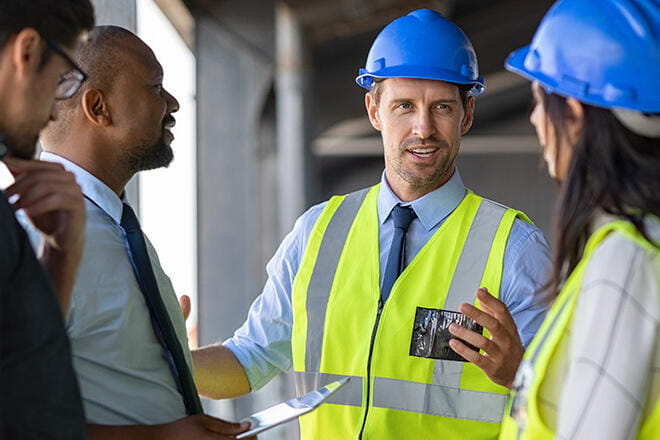 Happy mature engineer discussing the structure of the building with architects colleague at construction site.