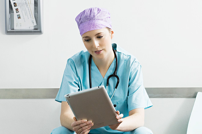 Doctor with blue scubes and purple hat holding an iPad
