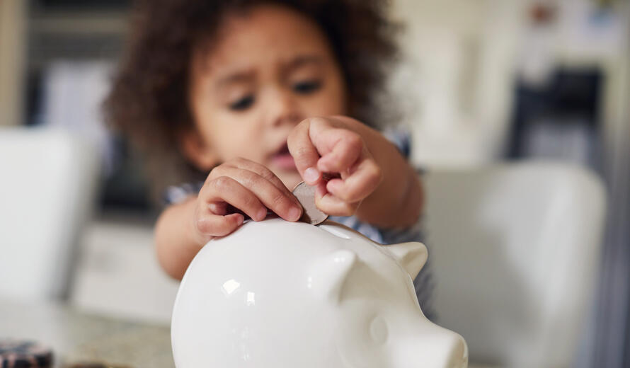 Little toddler girl saving money in her piggy bank.