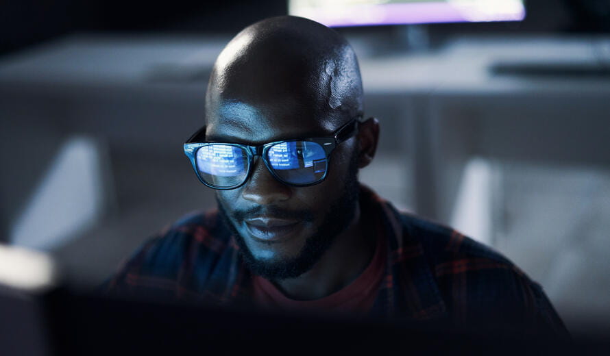 Software developer working late on computer with code reflected in glasses in a modern office