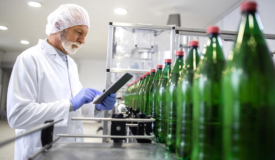 Quality control inspector checking green glass bottles on a beverage manufacturing production line.