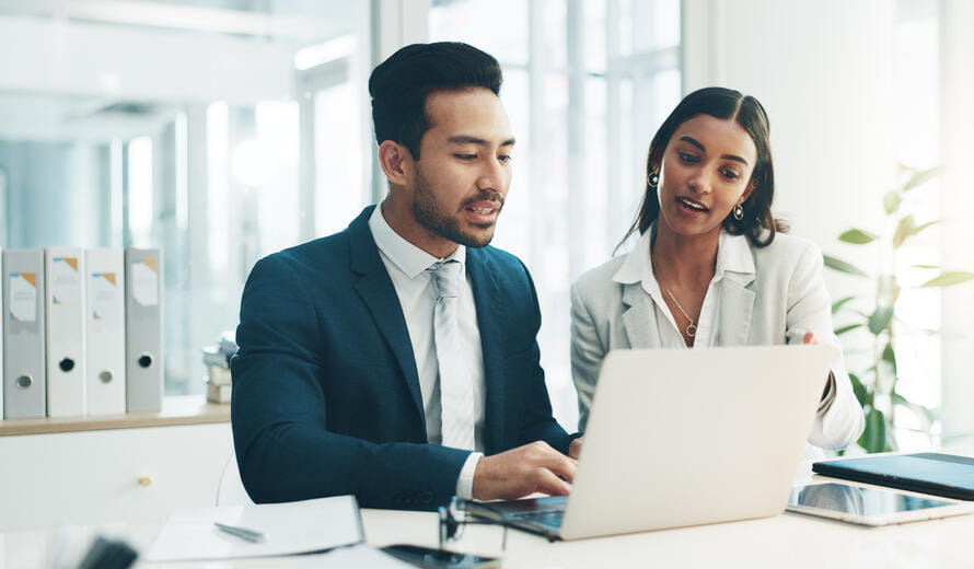 Stock photograph showing professionals collaborating at a desk using a laptop in an office environment.