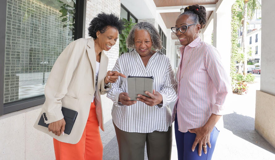 Three mature African American women look at a digital table.