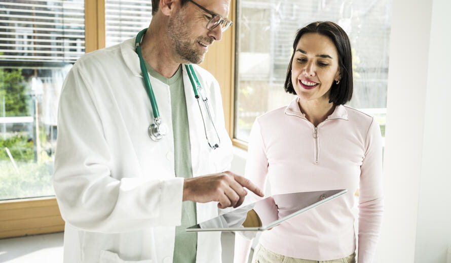 Healthcare professional discussing medical information on a tablet with a patient in a clinical setting