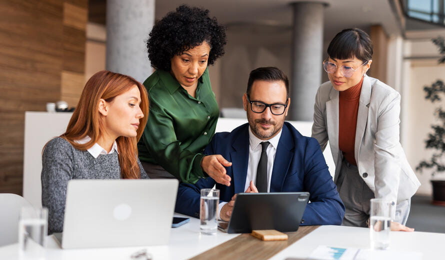 Professionals collaborate in a modern office environment with laptops and tablets.