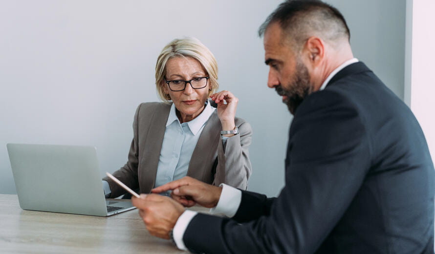 Shot of a two confident business persons sitting on a desk in the office and sharing ideas.