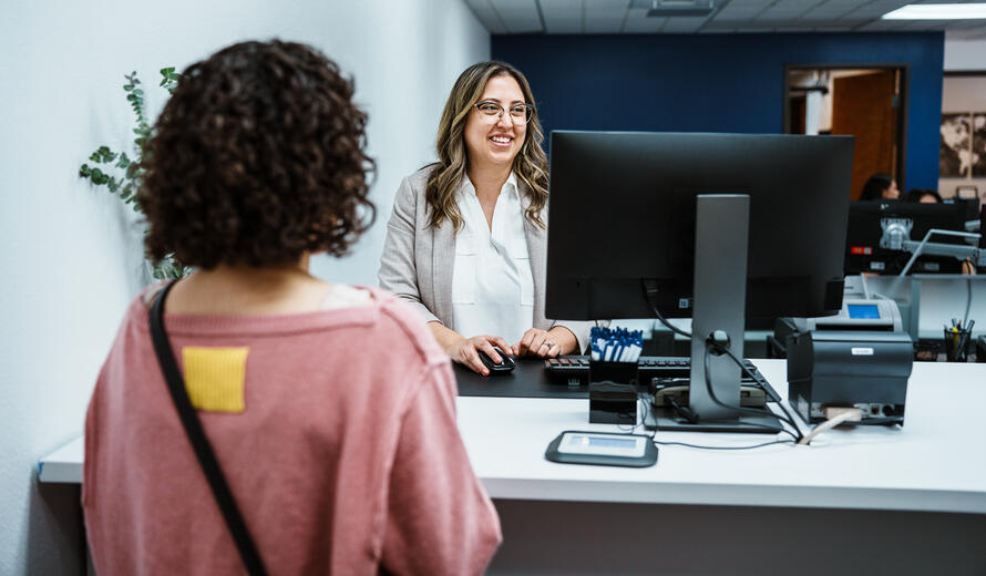 A smiling Latina teller speaks with a customer.