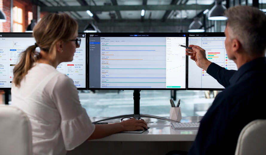 Two Professionals Discuss Integrated Cloud Software Solutions On Desktop Monitors.