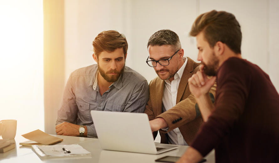 Three businessmen looking at a laptop.