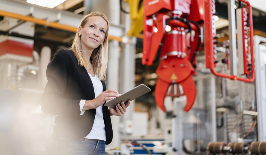 Smiling blond businesswoman looking away while holding digital tablet standing in factory