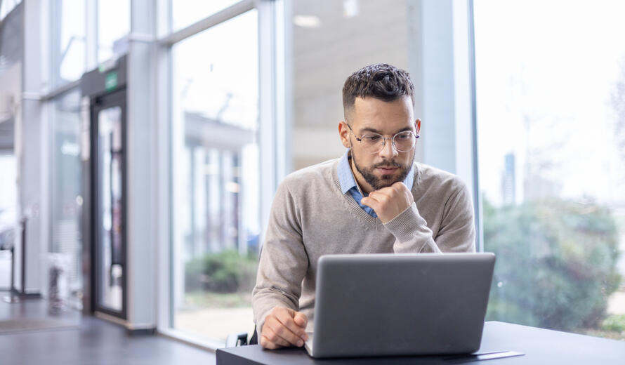 A man is deep in thought at his desk, surrounded by contemporary office ambiance with a laptop