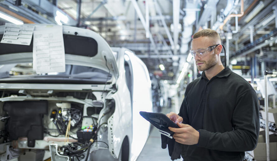 individual using a tablet on a manufacturing floor, representing digital processes, automation, and operational technology in an industrial environment.