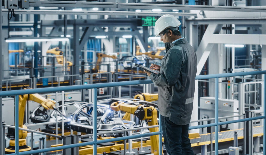 Multiethnic Car Factory Engineer in Work Uniform Using Tablet Computer.