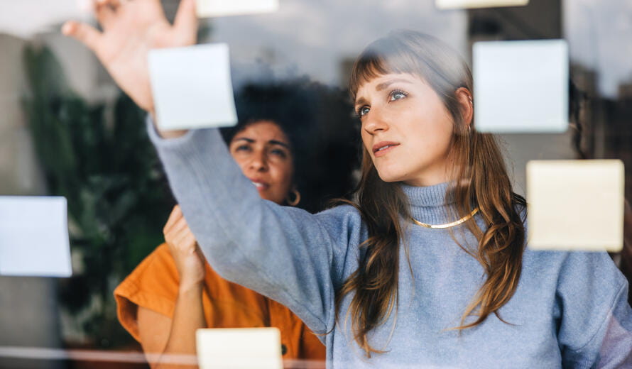 Creative businesswomen brainstorming using sticky notes. Young businesswomen discussing their business ideas during a meeting.
