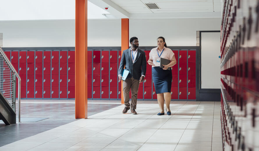 Two teachers walking through the school they work at in Gateshead, North East England. They are walking to their next class together while smiling and talking.
