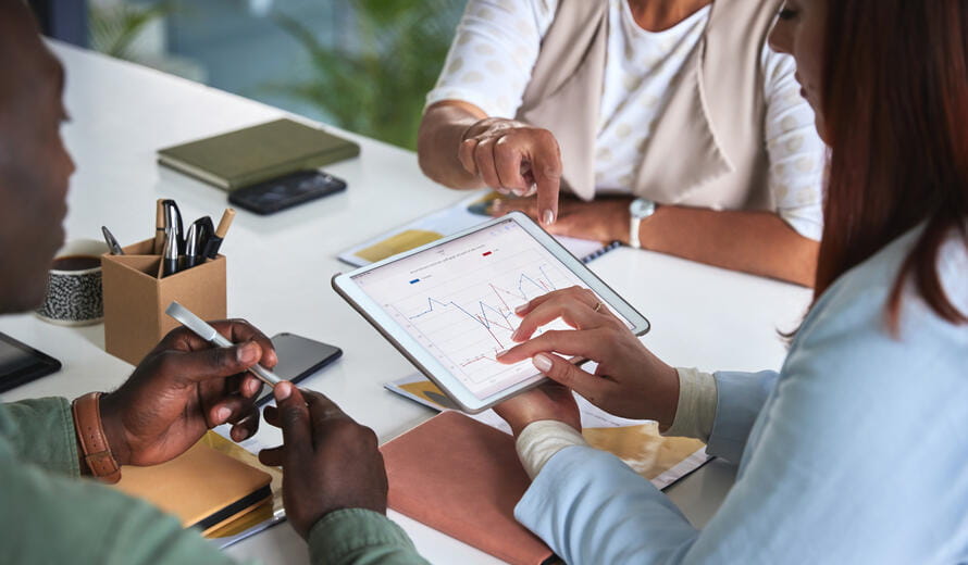 Business professionals review charts and statistics on a digital tablet during a meeting focused on financial planning and performance analysis.