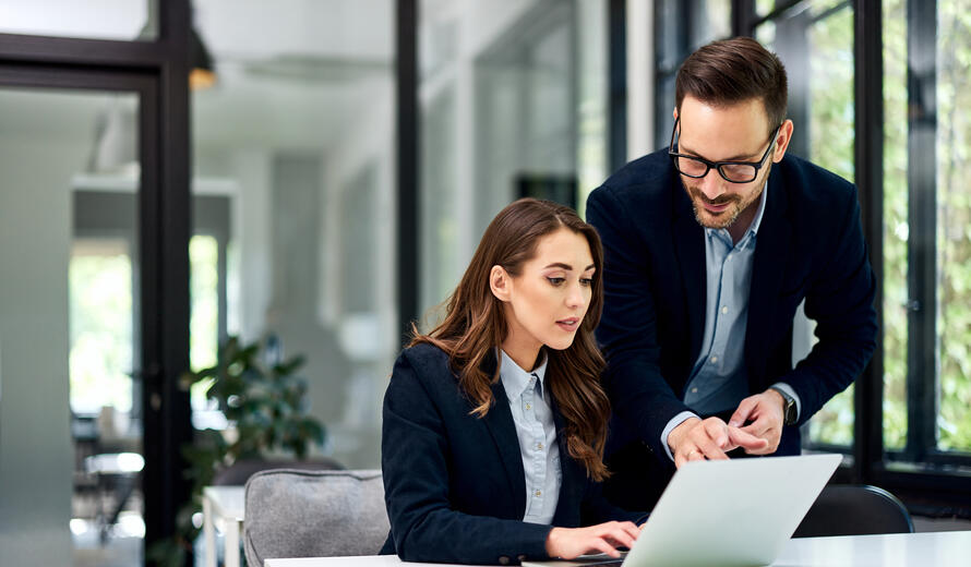 A pretty businesswoman sitting at the office table and working with a male colleague over a laptop.