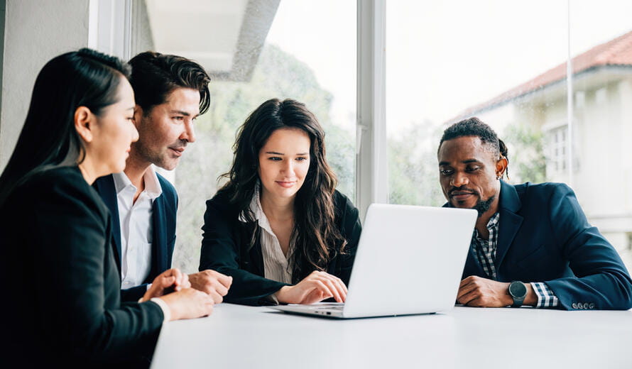 Diverse group of men and women in business collaborates in meeting room use laptop.