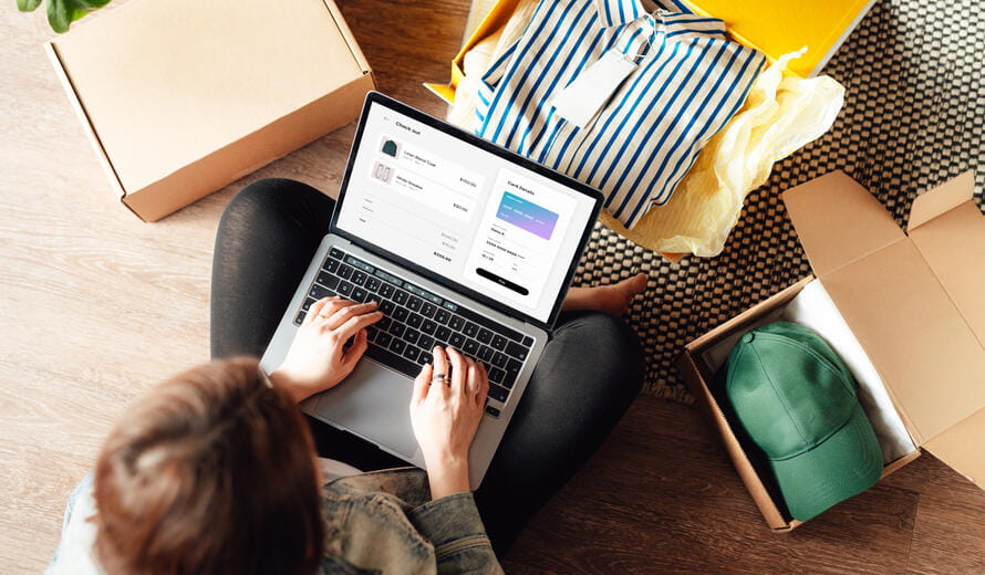 Elevated view of young woman making online payment via laptop while unboxing package from delivery. Online shopping and home delivery.