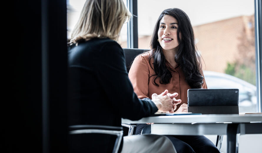 two female individuals engaged in a professional discussion in an office setting with a tablet on the table