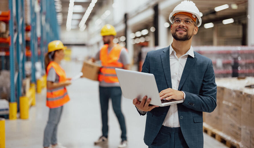 Portrait of warehouse manager working on laptop and checking shelves in warehouse.
