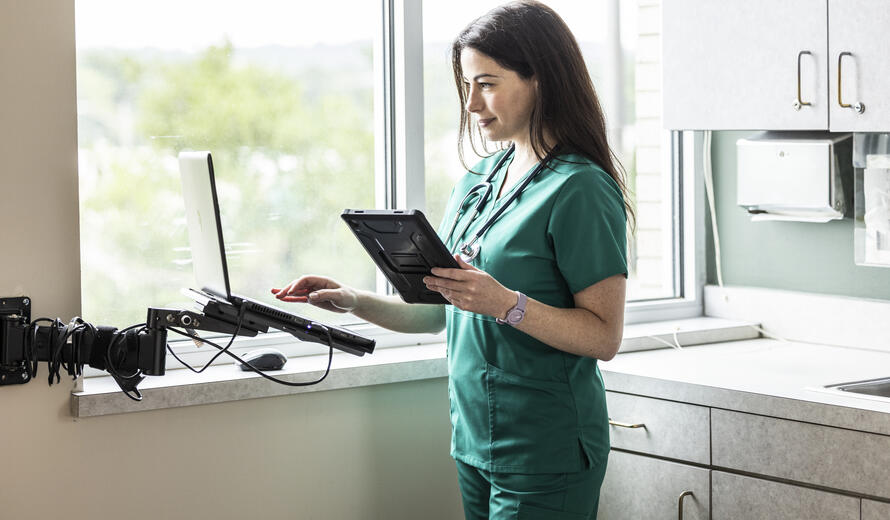 Female doctor wearing scrubs working on tablet in exam room