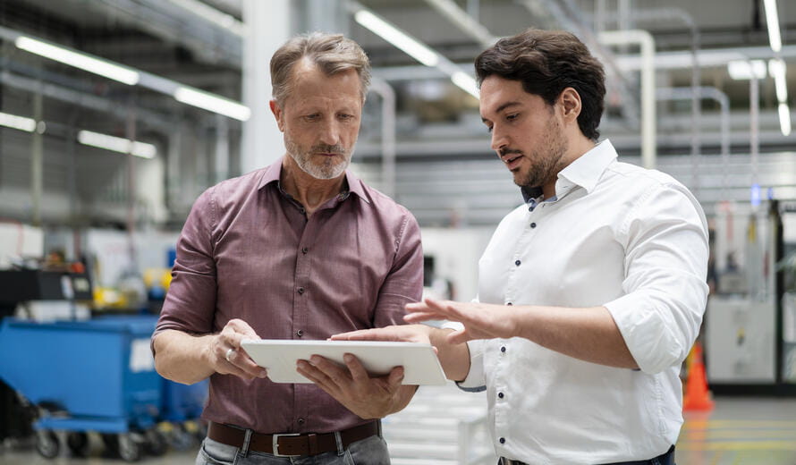 Business colleagues discussing strategies over tablet PC standing in factory