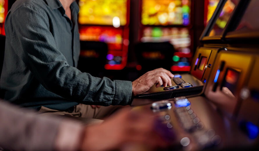 Close-up of a man operating a slot machine inside a lively casino with vivid lighting, showcasing recreational gaming in a vibrant setting, immersed in gambling and entertainment.
