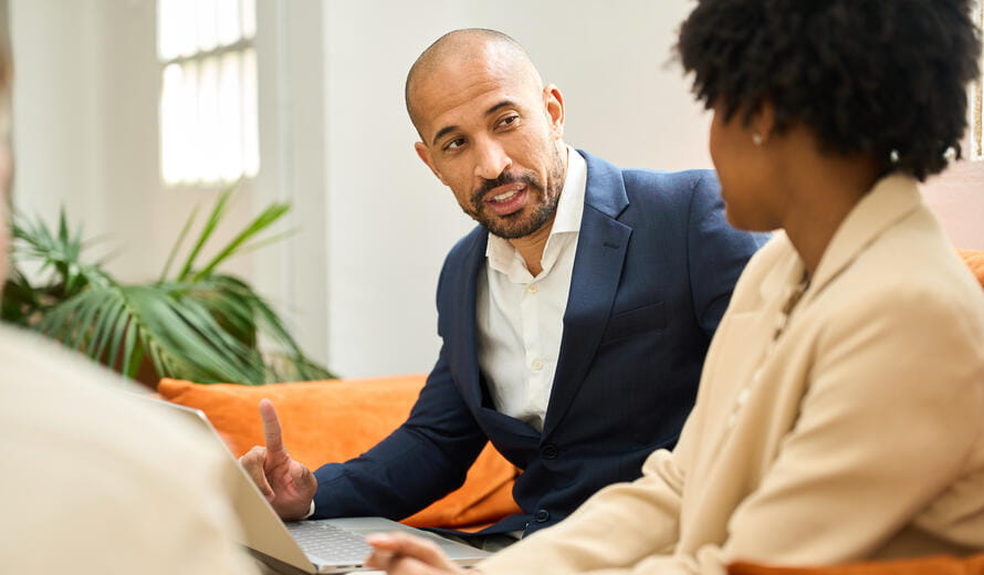 Financial advisor is explaining an investment strategy to his clients using a laptop in a coworking space