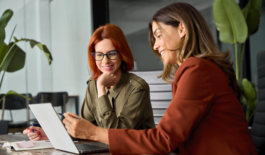 Two happy busy female employees working together using computer planning project.