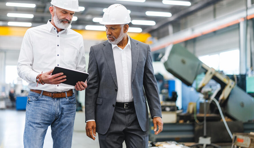manager and Caucasian engineer standing in a factory, reviewing workflow on a digital tablet.