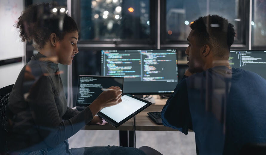 Two Software developers in modern office collaborating analysing the coding on computer screen. Colleague working together on the same codebase, discussing algorithms, and improving code quality. Code Review/Debugging, Analysing logic, identifying issues, and finding solutions in real-time.