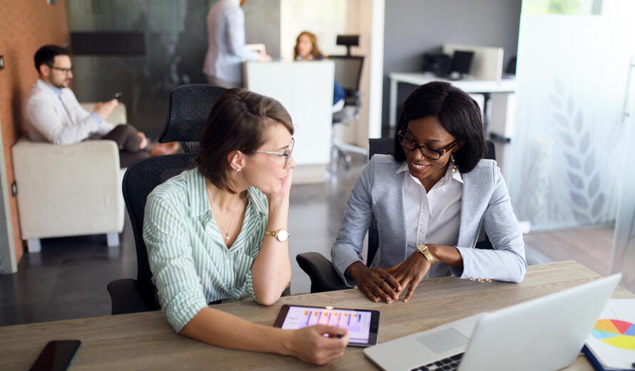 Business professionals using a digital tablet to analyze graphs in an office setting, showcasing teamwork and technology.