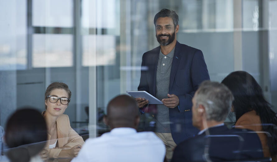 Business people dressed casual/corporate, talking together in large glass conference room