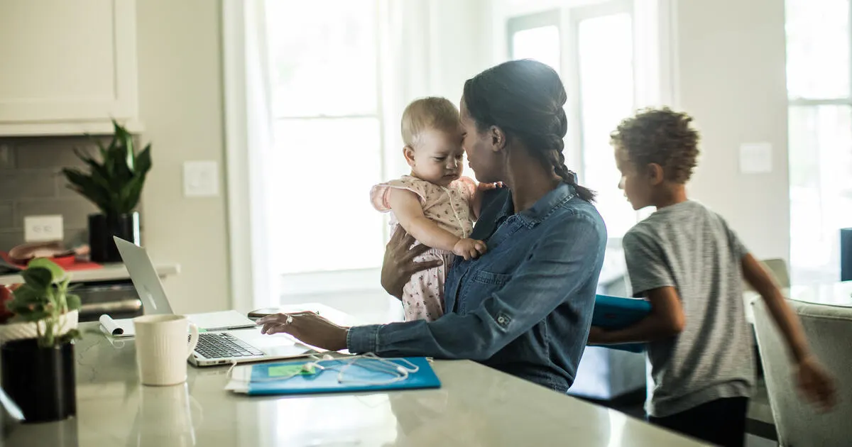 Mother holding baby while using laptop/working from home