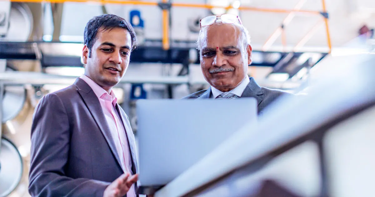 Senior Businessman Reviewing Production Progress Report on a Laptop at the Factory Floor with his manager.